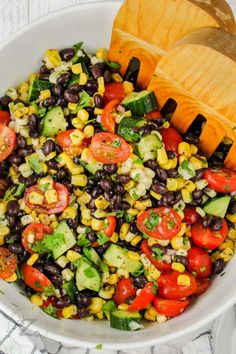 a white bowl filled with black beans, corn and avocado salad next to a wooden spoon