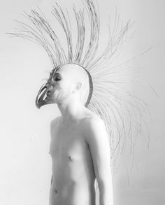 a shirtless man wearing a mask with feathers on it's head is standing in front of a white wall