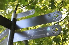 street signs pointing in different directions on a metal pole with trees in the back ground