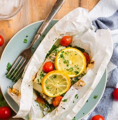 a white plate topped with fish covered in lemons and tomatoes next to a fork