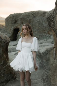 a woman in a white dress is walking through some rocks