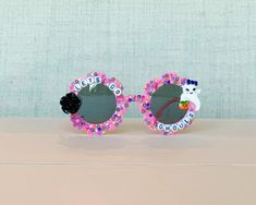 Bedazzled retro flower Halloween themed sunglasses perfect for any spooky lover.  Use these sunglasses to complete your Halloween outfit, Halloween theme party favors, or gift to any Halloween lover.  This listing provides 1 child pair (sized to fit most kids 3-8). These currently feature black pearl, champagne, pink, and purple rhinestones with a black rose and decorated ghost - please let me know if you wish for anything different.  Please note this is a made to order item and no two sunglasses will be the same.  Exact color and placement of gems will have slight variation. Ensuring your purchases arrive in perfect condition is important to me! Sunglasses are packaged in hard, sturdy boxes with crinkle cut packing paper.   All sunnies are shipped with a squeeze top soft leather case and Diy Sunglasses, Halloween Party Themes, Purple Rhinestone, Kids Sunglasses, Retro Flowers, Black Pearl, Black Rose, Flower Shape, Leather Case