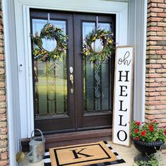 two wreaths are on the front door of a house with a welcome sign and potted plants