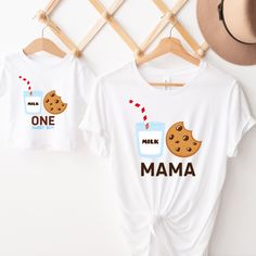 two t - shirts with cookies and milk on them hanging on a rack next to a hat