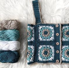 a crocheted bag sitting on top of a white rug next to balls of yarn