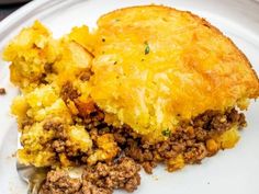 a white plate topped with a piece of pie covered in ground beef and cheese next to a fork