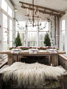 a long table with white fur on it in front of large windows and greenery