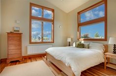 a bedroom with hardwood floors and three windows in the wall, along with a large bed