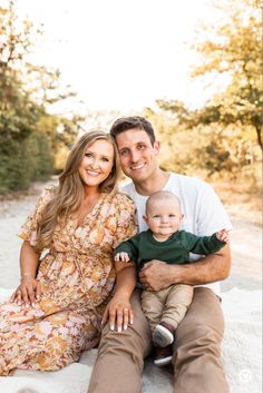 a man and woman sitting on the ground with a baby in their lap, smiling at the camera