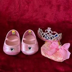 two pairs of princess shoes and a tiara on a red velvet surface with a pink background