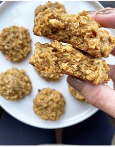 a person is holding up some cookies on a white plate and there are more oatmeal in the background