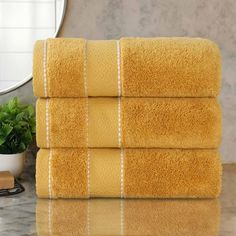 four yellow towels stacked on top of each other in front of a mirror and plant