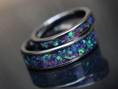 two wedding rings with black opal inlays on each ring, set against a dark background