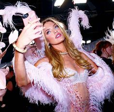 a woman in a pink feathered outfit takes a selfie with her cell phone