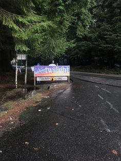 there is a sign on the side of the road in front of some trees and bushes