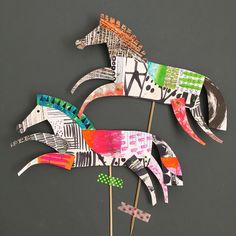 three paper horses are on top of toothpicks in front of a gray background