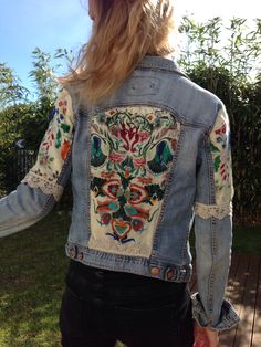 a woman wearing a jean jacket with embroidered designs on it's sleeves and back