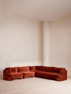 an orange couch sitting in the middle of a room next to a white wall and wooden floor