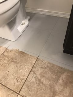 a white toilet sitting in a bathroom next to a wooden cabinet and tiled flooring