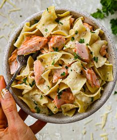 a hand holding a bowl of pasta with salmon and parsley on the side, ready to be eaten