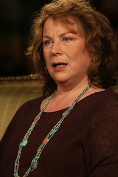 a woman sitting in a chair with a necklace on her neck and eyes closed, looking at the camera