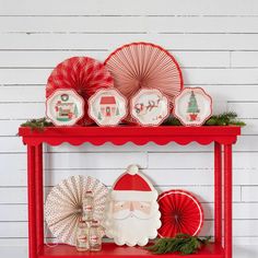 a red shelf filled with christmas decorations and paper plates on it's top, along with santa clause