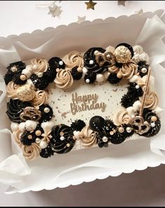 a birthday cake in a white box with black and gold decorations