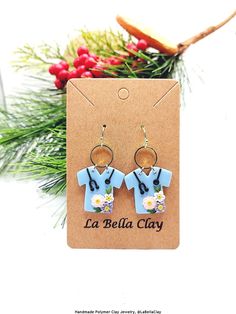 a pair of earrings with flowers on them sitting in front of a christmas tree branch