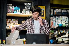 a man is talking on his cell phone while working at a laptop in a store