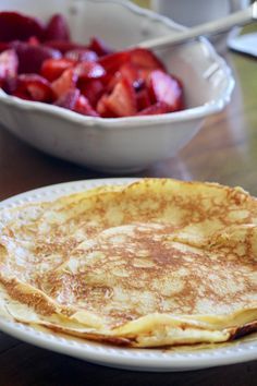 pancakes on a plate with strawberries in a bowl next to the same pancake