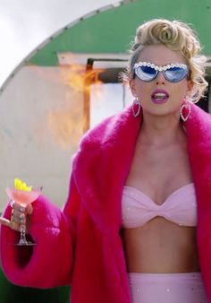 a woman wearing sunglasses and a pink fur coat holding a drink in her right hand