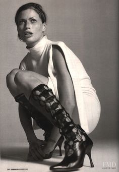 a black and white photo of a woman in high heel boots sitting on the floor