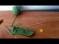 a green crochet bag sitting on top of a wooden table next to knitting needles