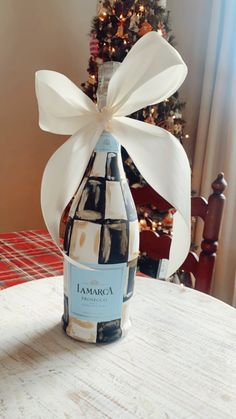 a wine bottle wrapped in white ribbon sitting on a table with a christmas tree behind it