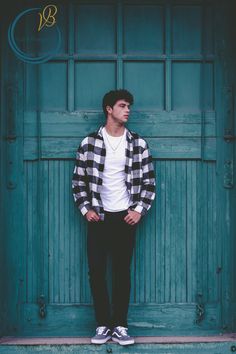 a young man standing in front of a green door with his hands in his pockets