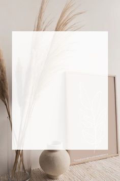 a vase with dry grass in it next to a white wall and an open book