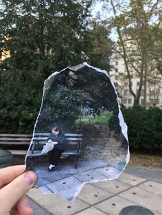 a person holding up a piece of paper with an image of a man sitting on a park bench