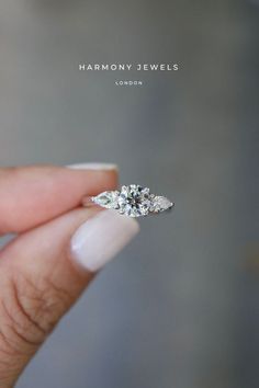 a woman's hand holding an engagement ring with three diamonds on it and the words harmony jewels