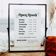 an open hours sign sitting on top of a wooden table next to a glass cup