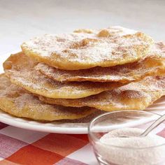 a stack of pancakes sitting on top of a white plate next to a bowl of sugar