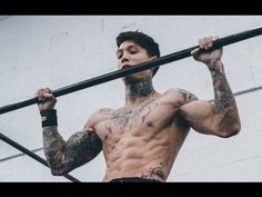 a shirtless man holding up a bar in front of his face and chest with tattoos on