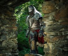 a man dressed as a knight standing next to a stone wall in a forest area