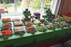 a green table topped with lots of trays filled with different types of food next to a window