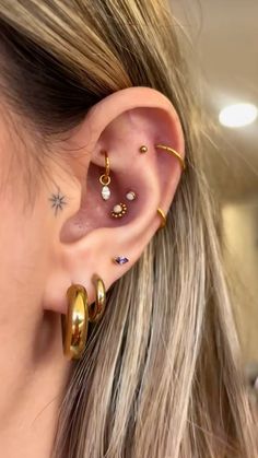 a woman wearing gold ear piercings with different colored stones on her left ear and the other side of her ear