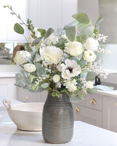 a vase filled with white flowers sitting on top of a counter next to a bowl