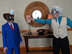 two people in costumes standing next to each other near a table with a mirror on it