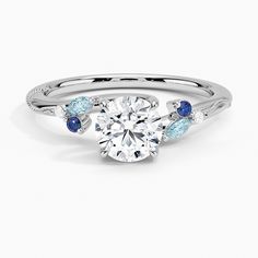 a diamond and blue sapphire engagement ring on a white background with the center stone surrounded by three stones