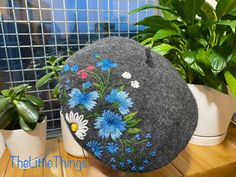 a gray hat with blue and white flowers is sitting on a table next to potted plants