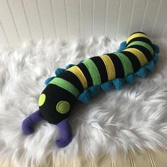 a stuffed caterpillar is laying on a fluffy white blanket with green and yellow stripes