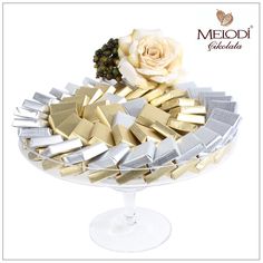 a white rose sitting on top of a cake plate filled with gold and silver pieces